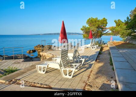 Des parasols et des chaises longues sont installés dans un lieu de baignade typique sur la côte de la ville de Krk, sur la mer Adriatique, en Croatie Banque D'Images