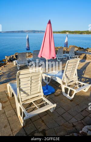 Des parasols et des chaises longues sont installés dans un lieu de baignade typique sur la côte de la ville de Krk, sur la mer Adriatique, en Croatie Banque D'Images