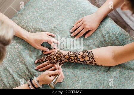 Mehndi artiste dessin floral henné tatouage sur la main de femme dans le salon de beauté. Maître appliquant le modèle traditionnel de mehendi pour la mariée avant le mariage. Banque D'Images