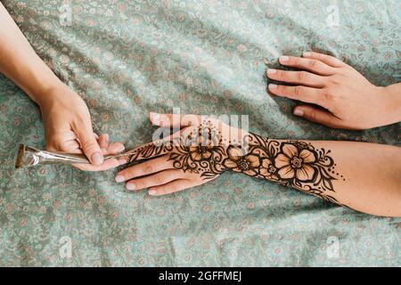 Vue de dessus art henné tatouage sur les mains des femmes. Maître artiste dessin arabe mehndi pour la mariée avant le mariage. Gros plan, vue de dessus. Motif fleuri. Cône Banque D'Images