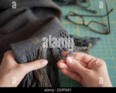 L'artisan est en action. La femme crée une frange sur un foulard ou un silencieux en laine. Mains d'artisan avec produit tissé Banque D'Images