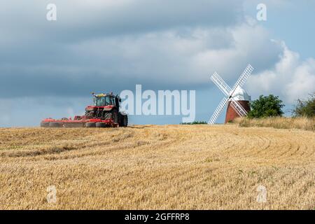 Halnaker Windmill dans le parc national de South Downs à West Sussex, Angleterre, Royaume-Uni, avec un tracteur rouge travaillant dans le champ de maïs, lors d'une journée ensoleillée d'été Banque D'Images