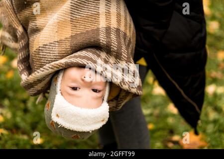 Jeune femme maman tenant bébé garçon fils à l'envers dans Orange Plaid à feuilles mortes jaunes Nice sourire regarder la caméra par temps froid en automne Banque D'Images