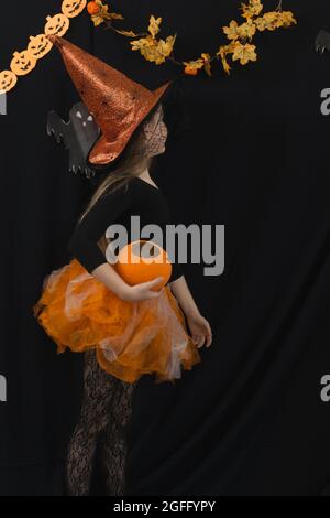 Une fille avec un citrouille de Jack et dans un costume de sorcière pour la célébration d'Halloween tourné au mur . Chapeau et jupe orange, blouse noire, voile toile d'araignée, Banque D'Images