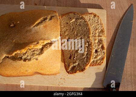 Un pain fraîchement cuit est coupé en morceaux, à côté d'un couteau sur une planche à découper en bois. L'authenticité des produits de boulangerie faits maison. Banque D'Images