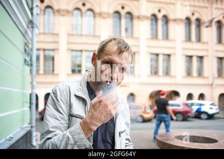 L'homme fume une cigarette électronique lors de la marche dans le centre-ville. Banque D'Images