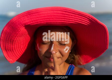 une adolescente en chapeau rose répandait de la crème solaire et riait. Banque D'Images