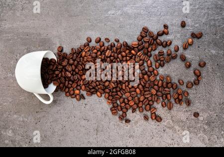 Tasse de café blanc renversée avec des grains torréfiés éparpillés Banque D'Images