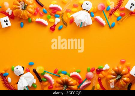 Joyeux motif Halloween. Bordure cadre faite de décorations d'halloween et de bonbons sur fond orange. Flat lay, vue de dessus, espace de copie. Banque D'Images