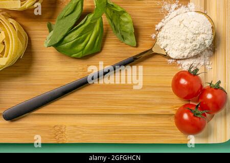 Vue de dessus image d'une cuillère avec farine, tomates cerises, basilic et table de bambou sur fond vert Uni Banque D'Images