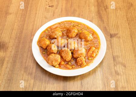 Plat principal de pain de viande cuit avec des légumes, des carottes et des petits pois en sauce sur une assiette blanche et une table en bois Banque D'Images