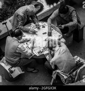 Quatre hommes chinois jouent avec des cartes à jouer dans une « zone de jeu » publique à WAN Chai, île de Hong Kong (monochrome) Banque D'Images