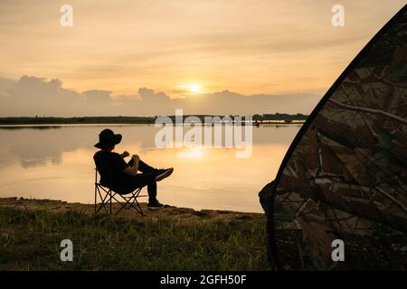 Jeune homme asiatique voyageur tenant une meuleuse en acier inoxydable pour moudre des grains de café avec manuel pour faire du café noir, profitant de la vue sur le coucher du soleil paysage de t Banque D'Images