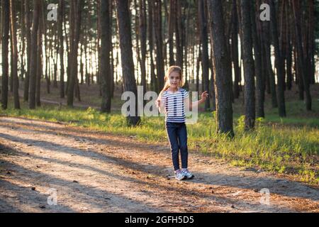 Une fille aux cheveux blonds court le long d'un chemin de forêt sautant sur toutes les branches le matin Banque D'Images