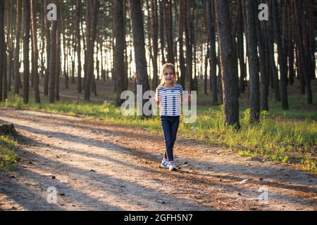 Une fille aux cheveux blonds court le long d'un chemin de forêt sautant sur toutes les branches le matin Banque D'Images