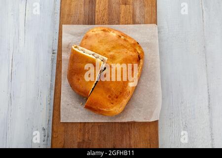 Du dessus, tarte à la viande coupée en miam servie sur parchemin sur planche à découper en bois sur table Banque D'Images