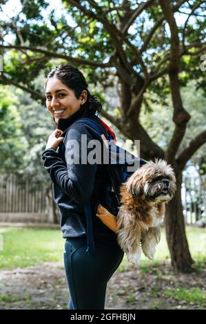 Une charmante jeune femme marche dans la nature, avec un sac à dos sur son épaule, d'où son chien sort. Concept relation et amour envers les animaux Banque D'Images