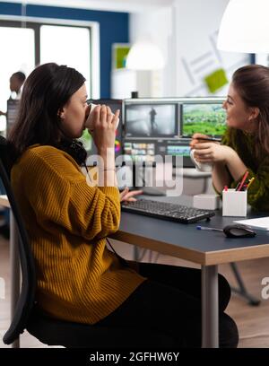 Une équipe de vidéastes travaillant en pause discuter et rire, buvant un café en travaillant dans l'application de montage sur pc dans une entreprise de multimédia numérique. Des femmes créatives qui éditent des films Banque D'Images