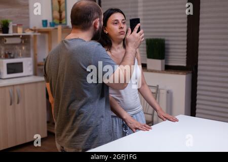 Un mari enragé et jaloux a triché par une femme malheureuse, un couple luttant à cause de messages texte secrets avec l'amant. Homme montrant smartphone avec preuve de tricherie à femme. Infidélité au mariage. Banque D'Images