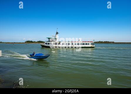 Ferry et un petit bateau à moteur en mouvement dans la lagune de Venise, en face de Torcello et de l'île de Burano. Venise, Vénétie, Italie, Europe. Banque D'Images