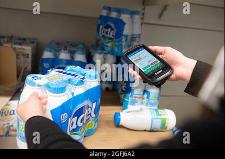 Supermarché Super U: Femme, préparateur de commande / emballeur sélection de produits dans une section du supermarché à l'aide d'un appareil mobile pour vérifier l'ordre du client Banque D'Images