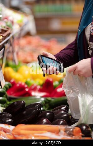 Super U supermarché: Femme, préparateur de commande / emballeur sélection de produits dans le département des fruits et légumes d'un supermarché en utilisant un appareil mobile à c Banque D'Images