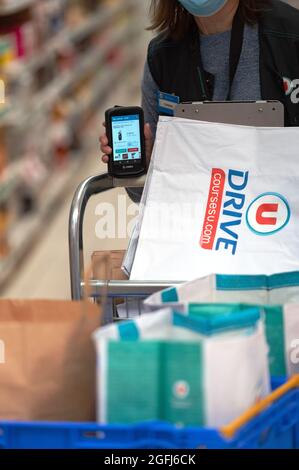 Supermarché Super U: Femme, préparateur de commande / emballeur sélection de produits dans une section du supermarché à l'aide d'un appareil mobile pour vérifier l'ordre du client Banque D'Images