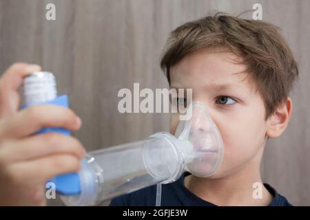 Enfant garçon utilisant un spray médical pour respirer. Inhalateur, espaceur et masque. Vue latérale Banque D'Images