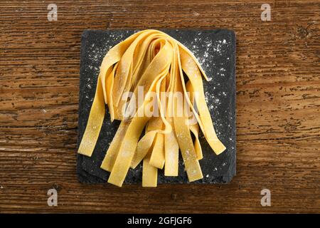 Vue de dessus des pâtes italiennes traditionnelles crues faites maison sur une plaque d'ardoise noire parsemée de farine sur une table en bois Banque D'Images