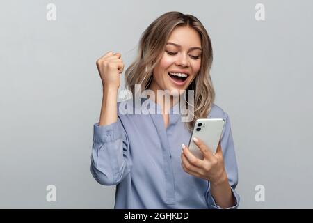 Une jeune femme surjoyeuse célèbre le succès en levant le poing et en disant oui en tenant le smartphone à la main Banque D'Images