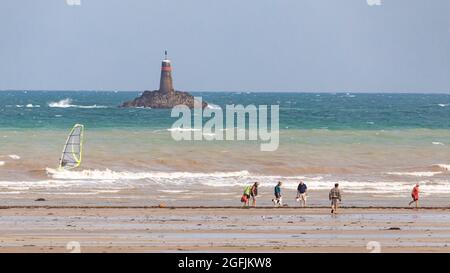 Plouha (Bretagne, nord-ouest de la France): Randonneurs et conchyliculteurs marchant pieds nus dans l'eau et surfeurs sur les vagues, plage "plage de l'" Banque D'Images