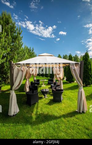 Belvédère en toile blanche avec meubles de jardin en plastique dans une pelouse verte d'été. Vertical, espace de copie. Banque D'Images