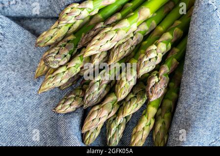 Gros plan bouquet d'asperges vertes fraîches récoltées en saison sur fond de cuisine en tissu rustique bleu. Gourmet végétalien sain Banque D'Images