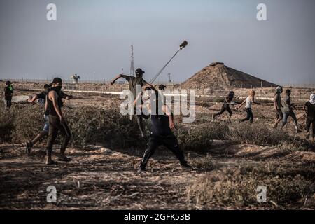 Gaza, Palestine. 25 août 2021. Un manifestant palestinien utilise un coup de feu pour lancer des pierres sur l'armée israélienne lors d'une manifestation près de la frontière entre Israël et la bande de Gaza. Une marche a été organisée par les factions palestiniennes à la frontière entre la bande de Gaza et Israël pour protester contre la poursuite du siège imposé à la bande de Gaza et à Israël. L'entrée de matériaux de construction dans la bande de Gaza a été retardée pour rebâtir les vestiges de la dernière agression en mai dernier. (Photo de Yousef Masoud/SOPA Images/Sipa USA) crédit: SIPA USA/Alay Live News Banque D'Images