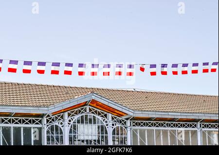 Drapeaux français agitant dans le vent au-dessus du toit de la Halle de Saint-Cyprien à l’occasion du 14 juillet, jour férié français. Banque D'Images