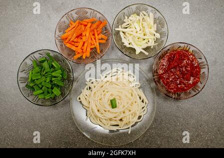 Préparation de nouilles Veg Schezwan Hakka qui comprend des nouilles cuites, des légumes frais et de la sauce schezwan sur fond gris Banque D'Images