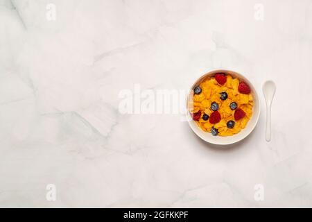 Petit déjeuner du matin bol de céréales de céréales de céréales de céréales de céréales sur une surface en marbre blanc avec framboises et bleuets dans un bol blanc avec une cuillère blanche.Copier l'espace Banque D'Images