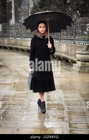 Une jeune femme d'affaires avec un parapluie dans son manteau va au travail par temps pluvieux Banque D'Images