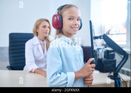 Joyeux jeune fille dans les micro-casques/oreillettes qui subissent une procédure de dépistage de l'audition Banque D'Images