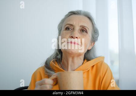 Une femme âgée à cheveux gris boit du café tout en étant assise à la maison. Bonne retraite Banque D'Images