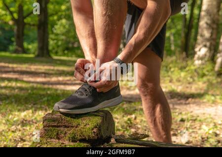 Le sportif enfile les lacets de ses jambes dans des baskets gros plan l'athlète court dans le parc à l'extérieur, autour de la forêt, les arbres de chêne vert herbe youn Banque D'Images