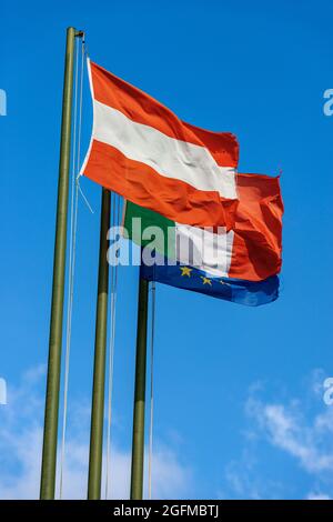 Drapeaux autrichiens, italiens et de l'Union européenne avec mât, soufflant de la goretherness dans le vent sur un ciel bleu clair avec des nuages et de l'espace de copie. Banque D'Images