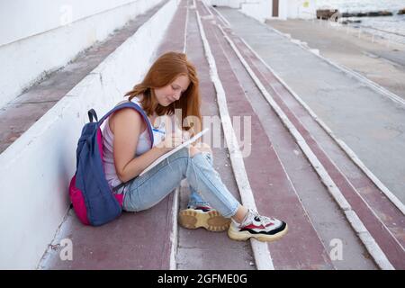 adolescente dessine dans le carnet d'esquisses tout en étant assis sur les marches. Banque D'Images