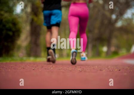 Jeune couple de sport de forme garçon et fille courant pendant faire de l'exercice sur les pistes rouges du stade public à l'extérieur Banque D'Images