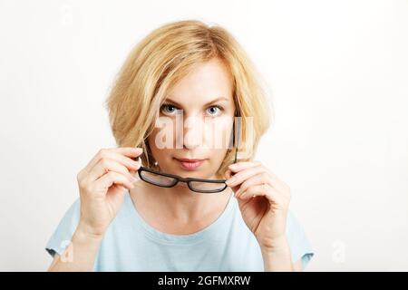 Gros plan portrait d'une femme prend ses lunettes et regarde directement dans l'appareil photo. Arrière-plan clair avec espace de copie. Banque D'Images