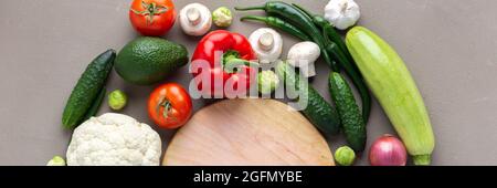 Bannière de légumes frais biologiques de ferme, concept de nourriture saine, légumes et champignons autour d'une planche à découper ronde sur fond gris Banque D'Images