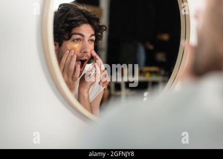 homme homosexuel appliquant des cellules oculaires et regardant le miroir Banque D'Images