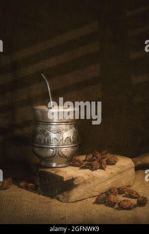 Coupe verticale de tasse à découper argentée avec paille pour s'accoupler sur un morceau de bois abîmé et des noix autour Banque D'Images