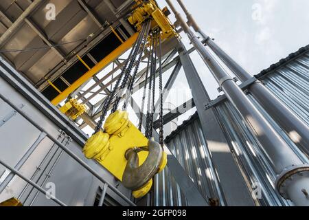 Pont roulant industriel avec une chaîne et un gros crochet jaune à l'usine. Mécanisme de levage Banque D'Images