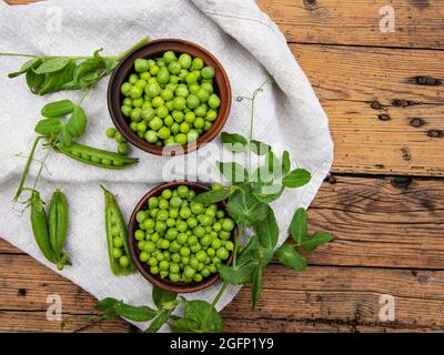 Petits pois verts frais dans un bol en céramique, gousses, sur la table, vue de dessus, graines Banque D'Images